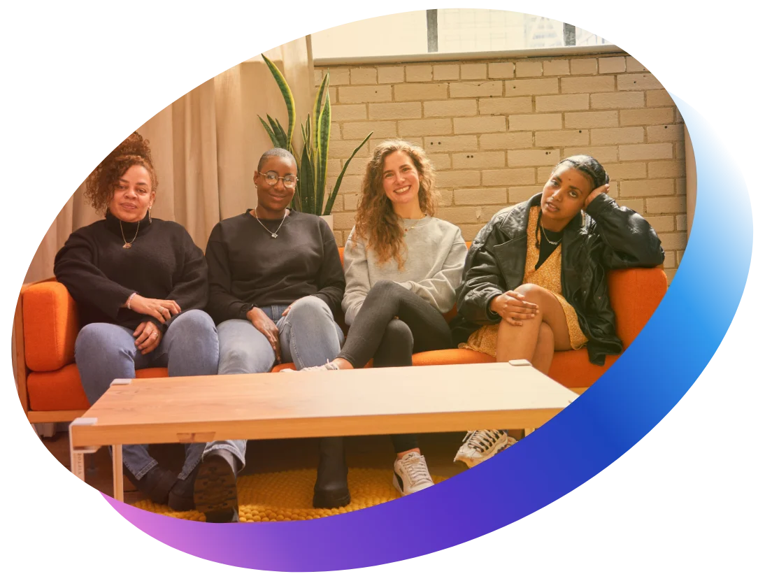four women sitting together on an orange couch in a modern lounge area, smiling and relaxed
